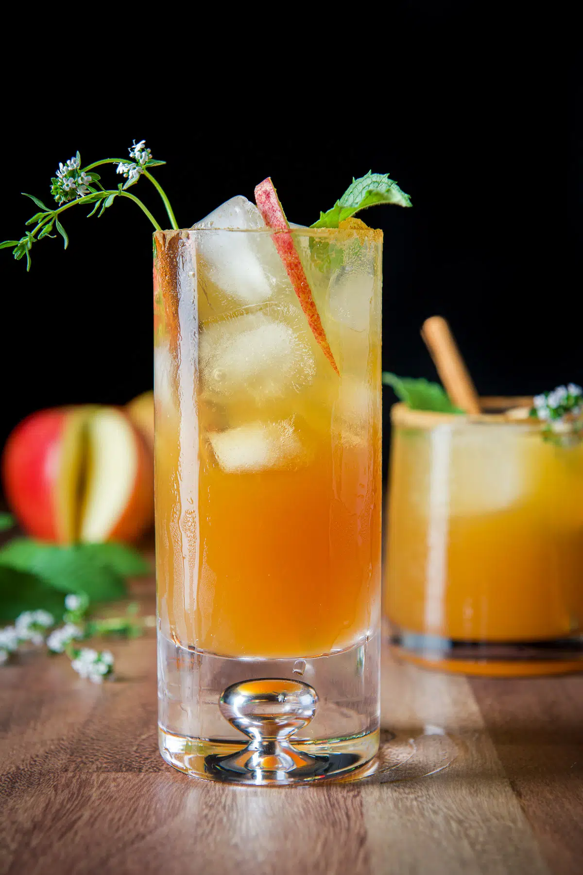 Tall glass with the apple cider drink in it with mint, thyme, and apple slices garnish