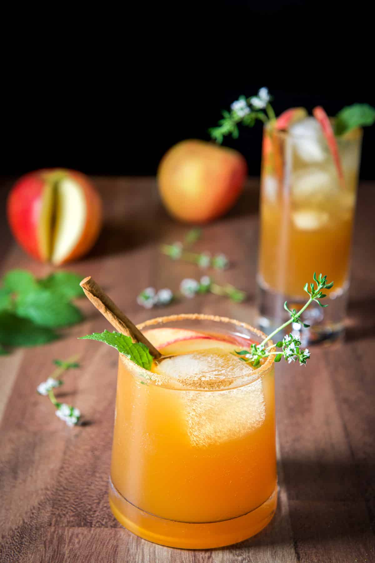 Short glass in front of a tall glass filled with the apple spritzer