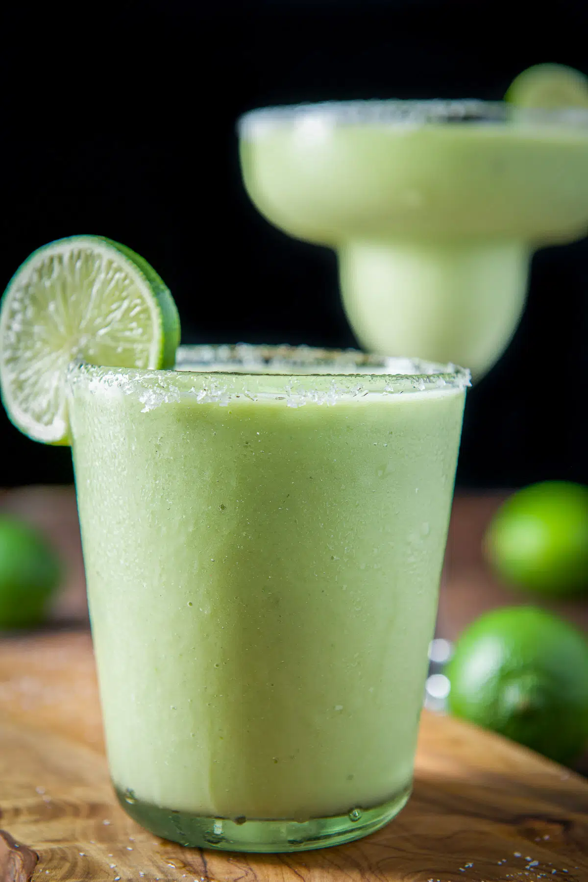 Vertical view of a short glass with the avocado margarita in it with salt and lime wheels on the rim