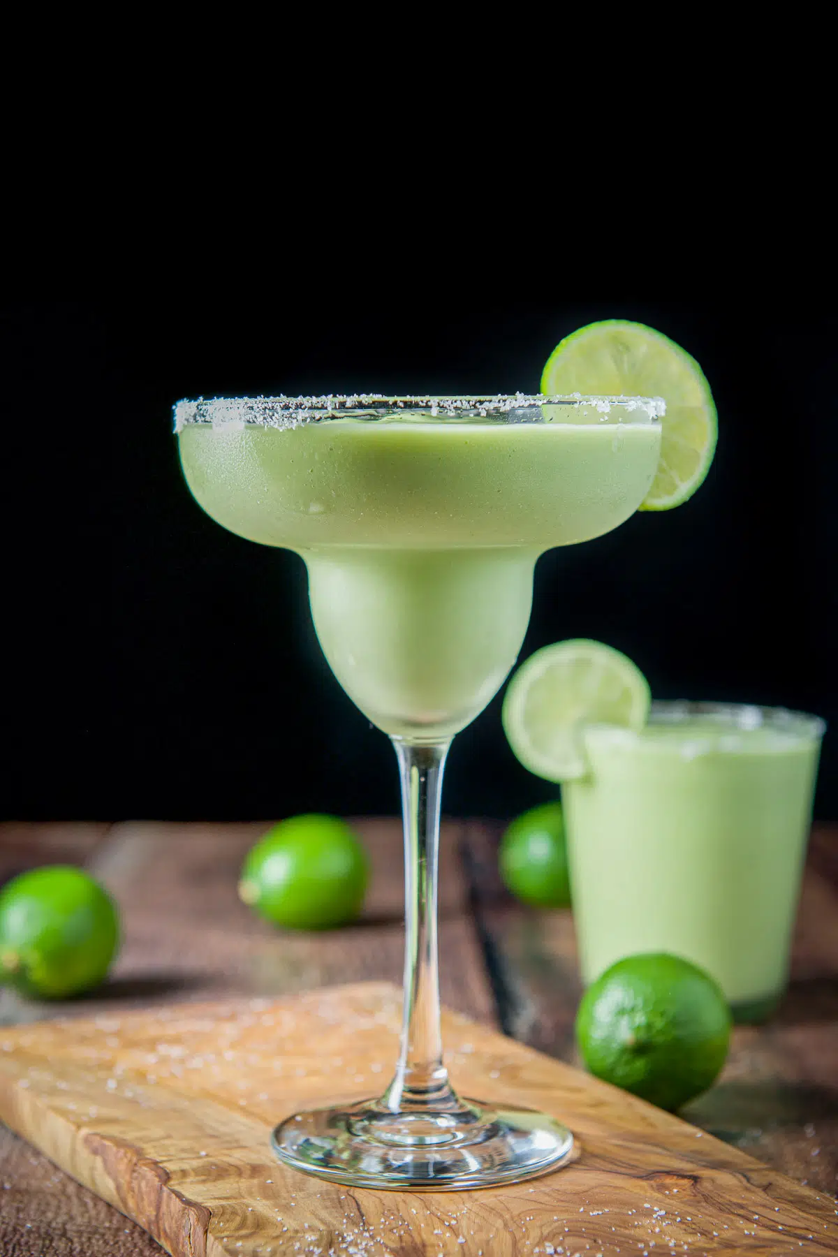 Vertical view of a creamy green drinks with limes on the board