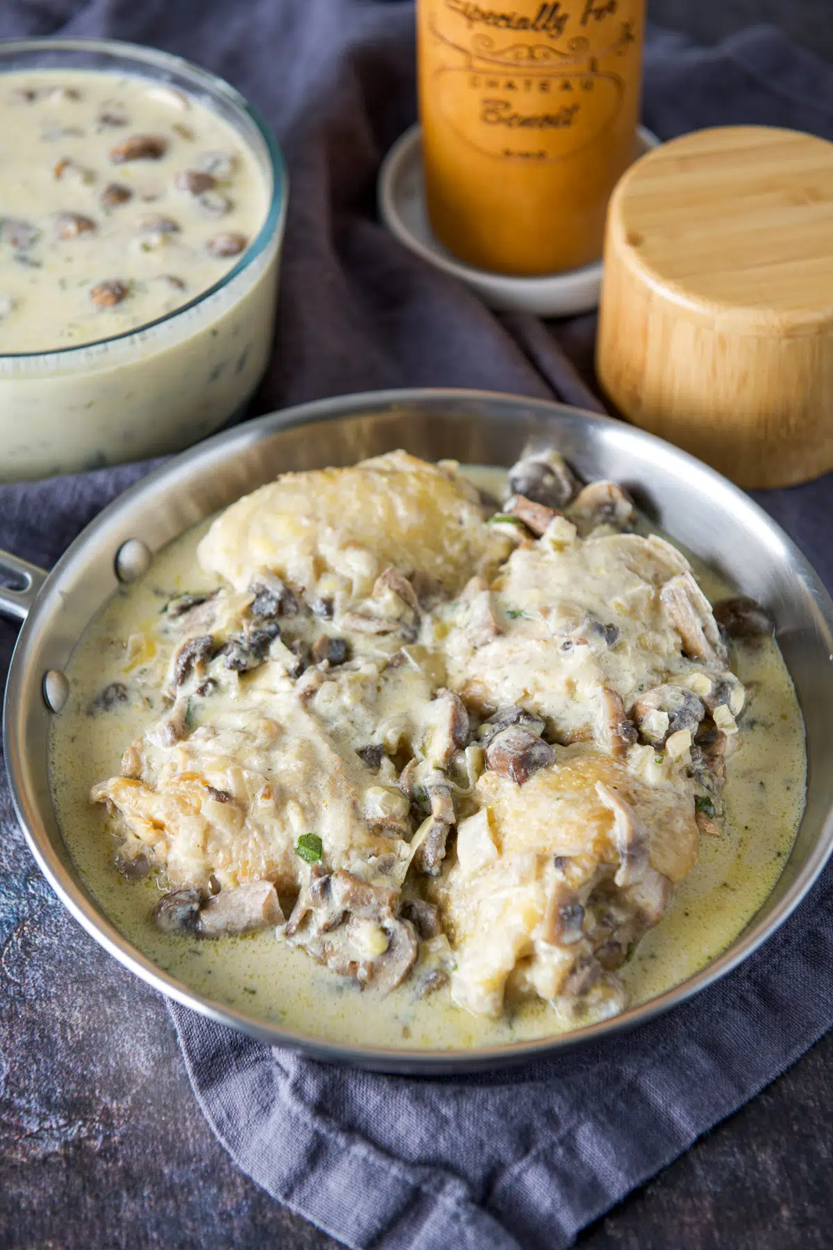 A steel pan with four chicken thighs, with the creamy sauce and extra sauce in the back