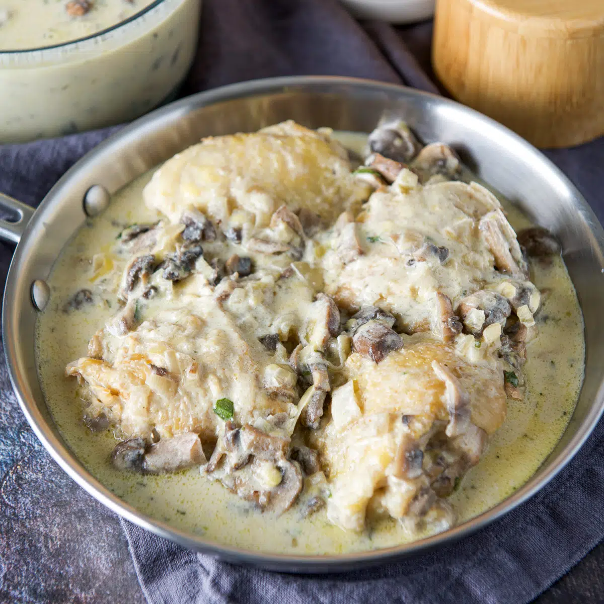 Square photo of a pan with chicken thighs and a mushroom sour cream sauce
