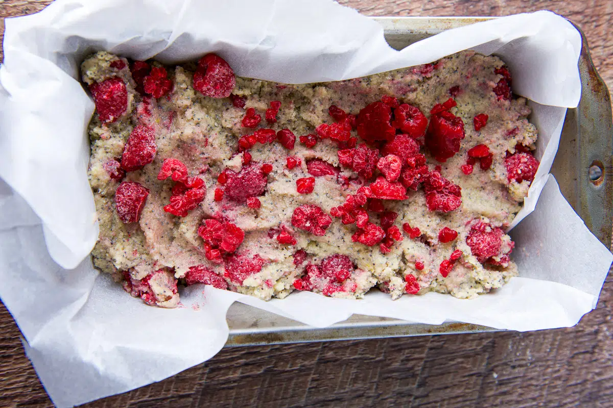 sweet bread batter in a parchment paper lined pan with raspberries on top