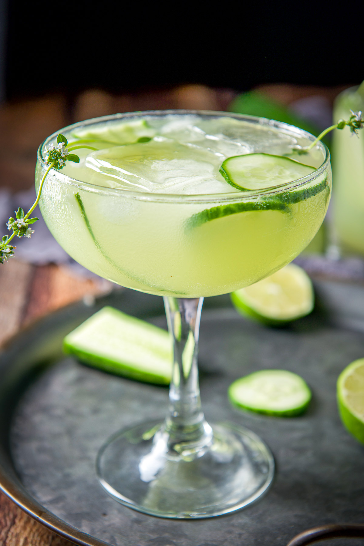 A bowl glass filled with the green margarita with fresh thyme and cucumbers as garnish