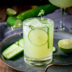 A cucumber margarita in a glass with cucumber and lime as garnish - square