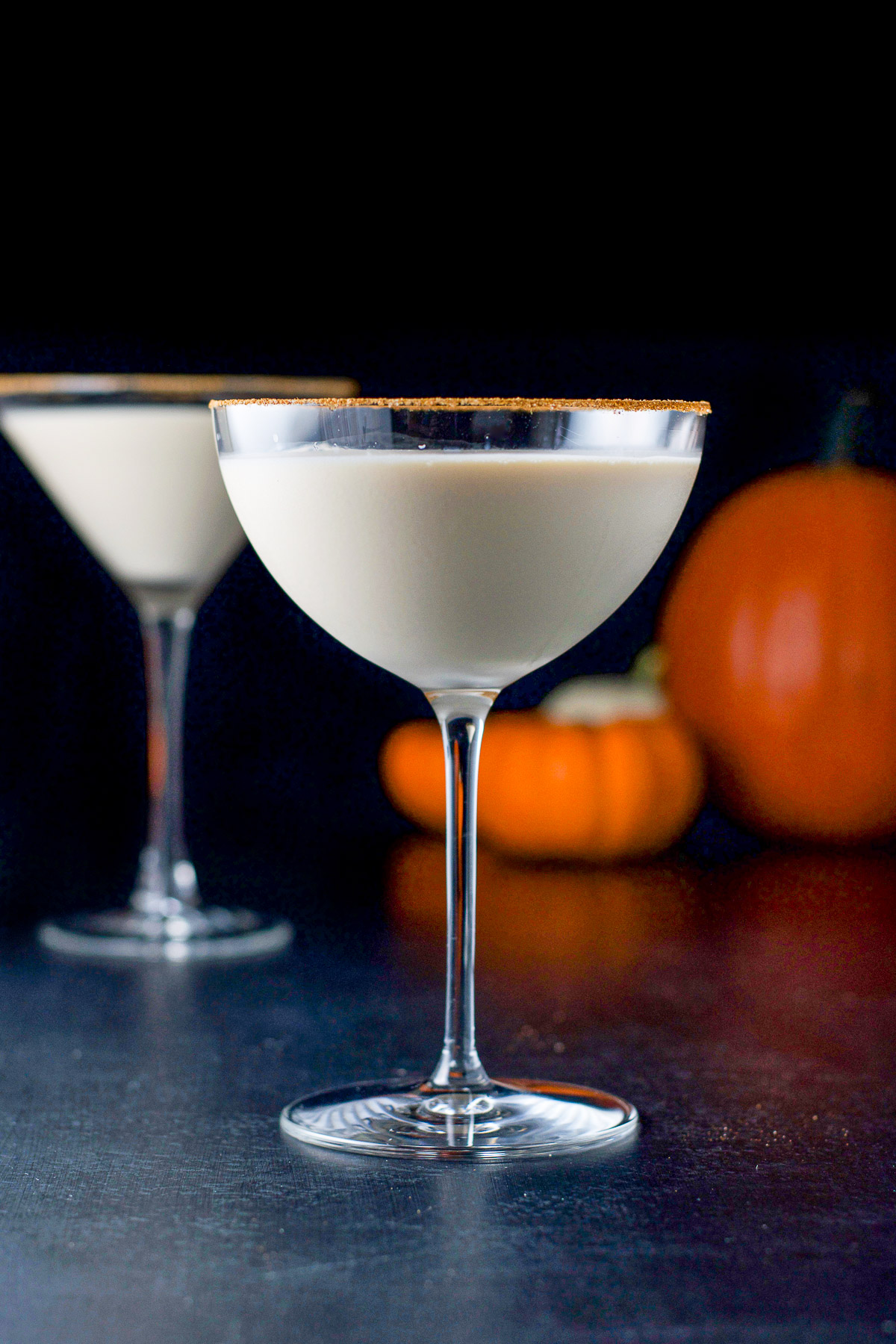vertical view of the creamy cocktail in martini glasses with pumpkins in the back