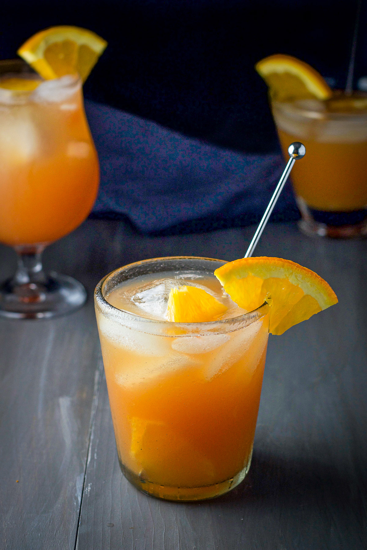 Double old fashioned glass filled with the swizzle with a stirrer in it with two glasses in the back