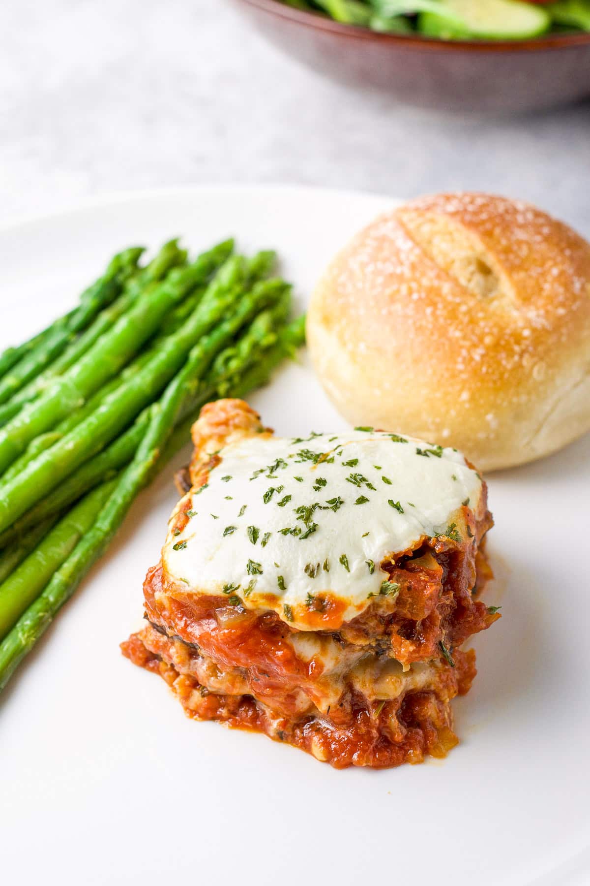 Close up view of a square of layered parm on a plate with asparagus and roll