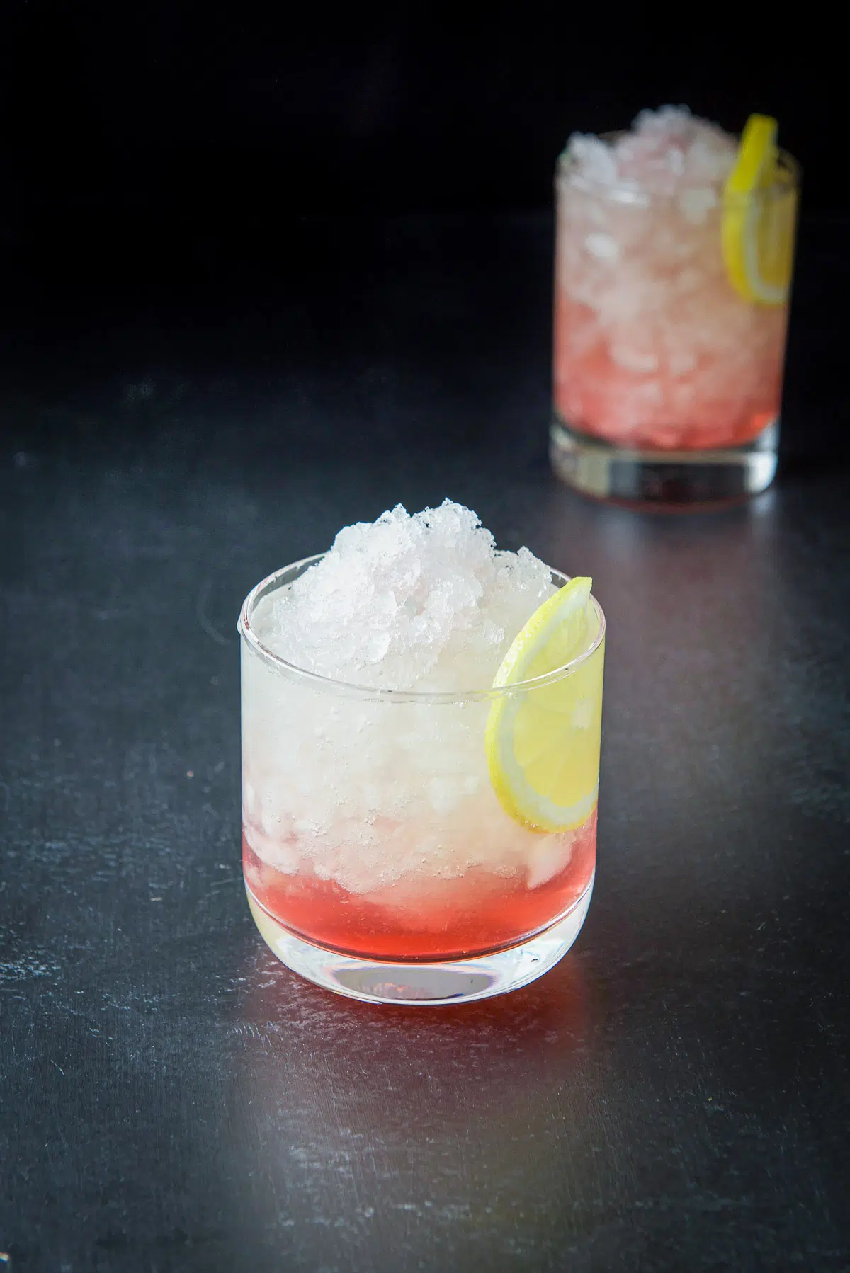 Short glass filled with ice, a red cocktail and lemon slice