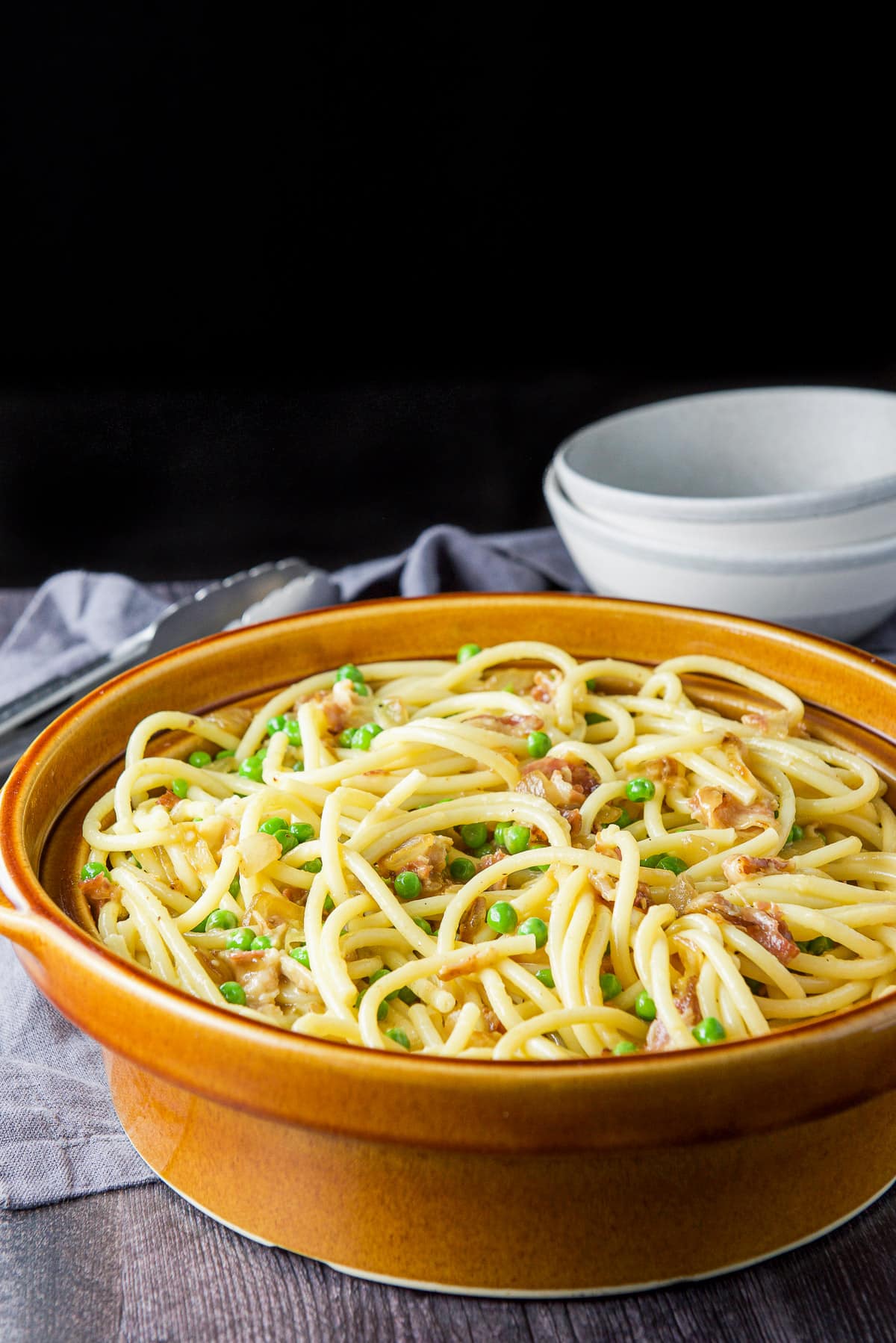 Big brown bowl filled with the carbonara with two grey bowls behind