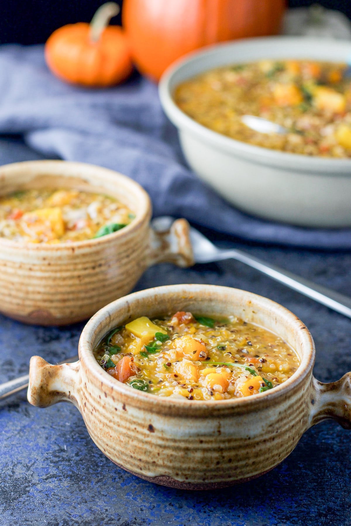 Close up of a brown crock filled with the squash stew with another crock and serving bowl behind it