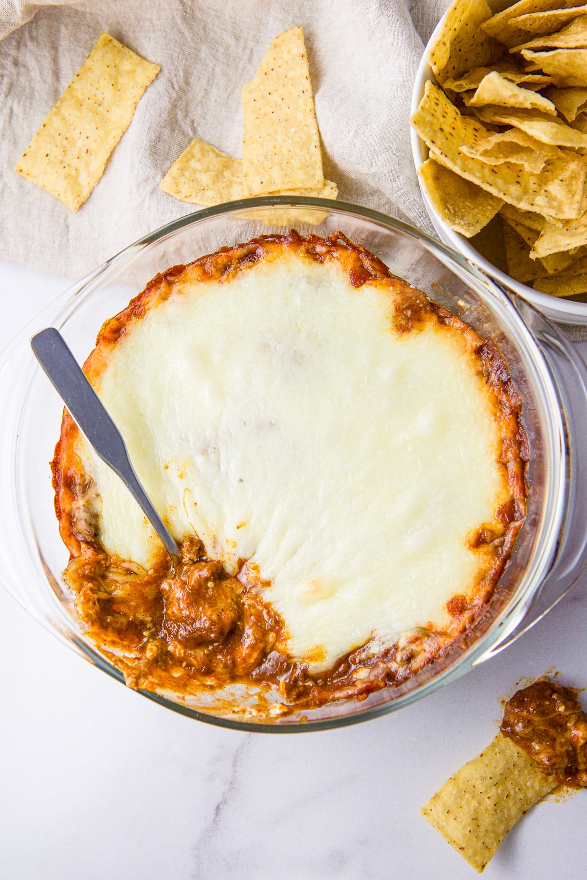 Overhead view of a casserole dish with a spoon in it and a chip with the dip on the side