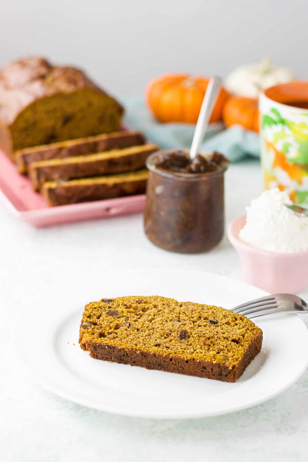 A white plate with a slice of sweet bread on it with the rest of the bread in back