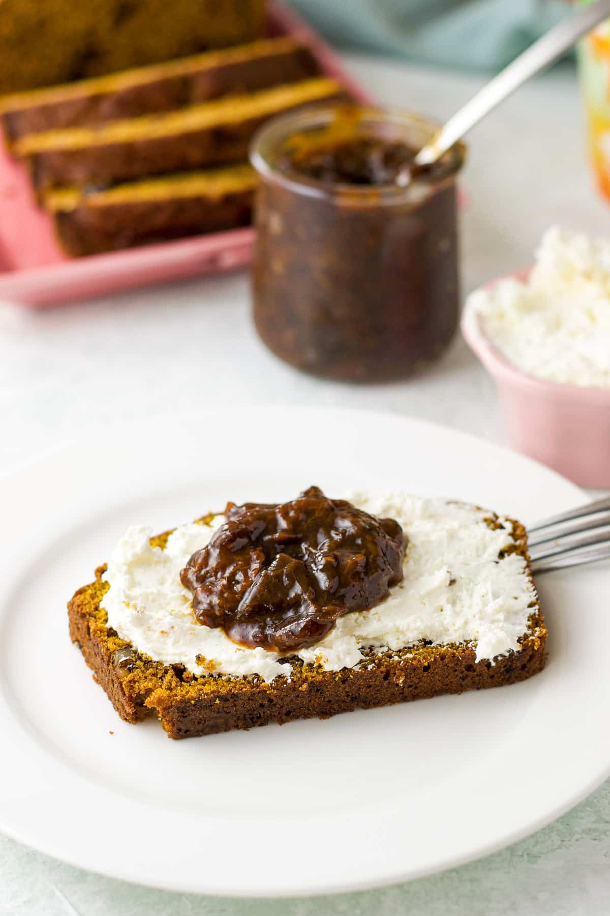 close up of a white plate with a piece of sweet bread slathered with cream cheese and jam
