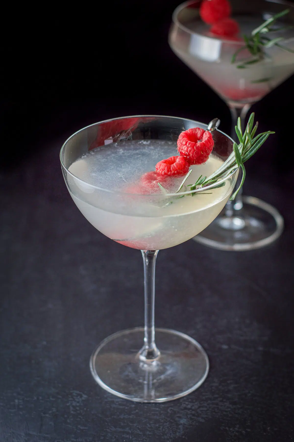 Higher view of the drinks in martini glasses with rosemary and raspberries as garnish