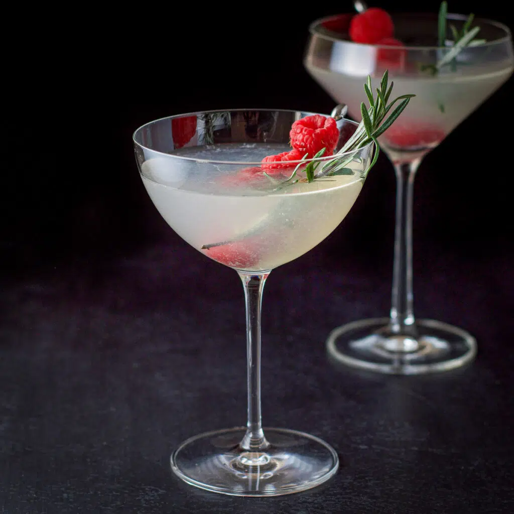 Bowl and curved martini glasses filled with the mistletoe martini with raspberries and rosemary in as garnish