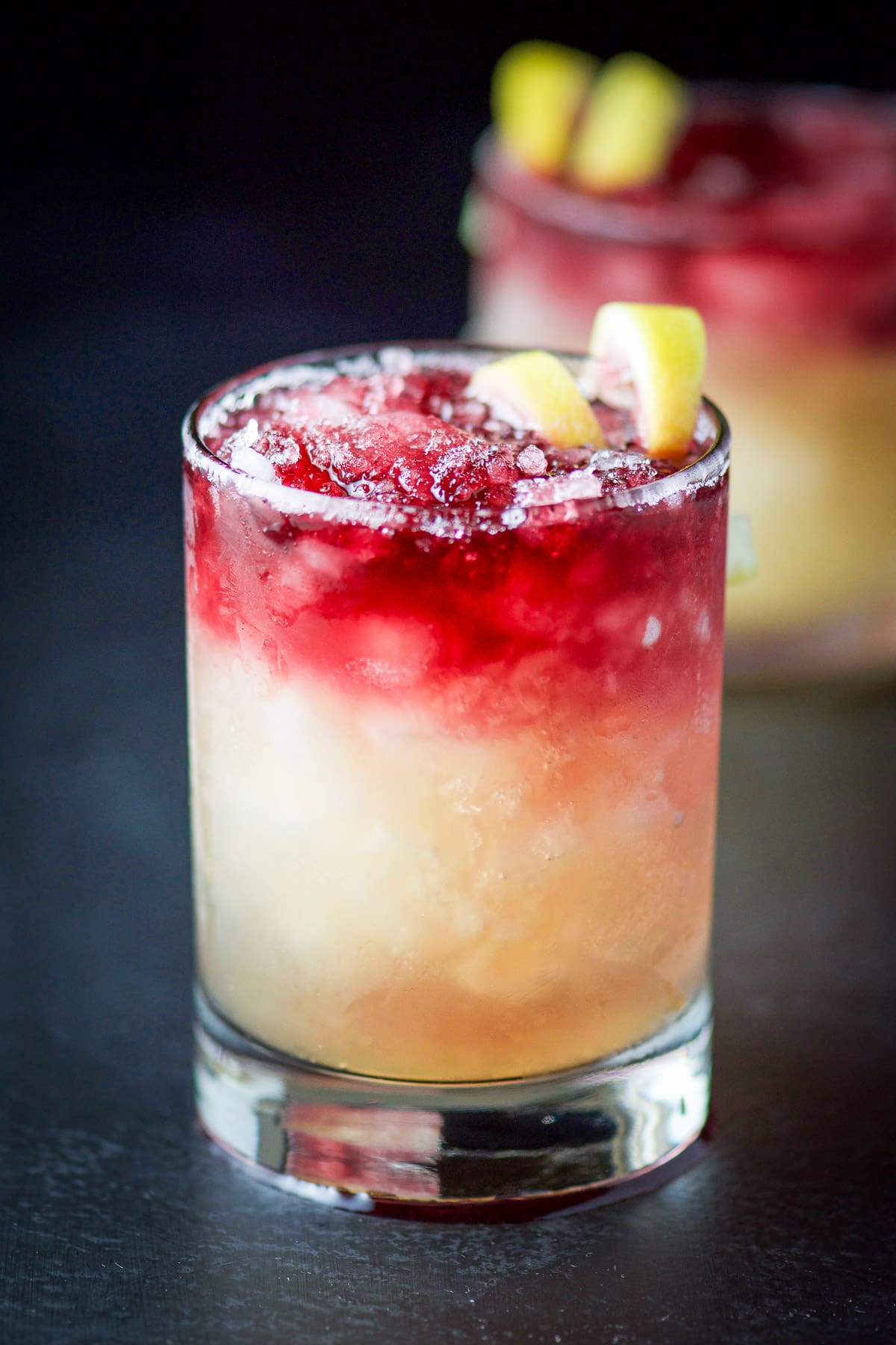 A double old fashioned glass with wine and a sour cocktail in it