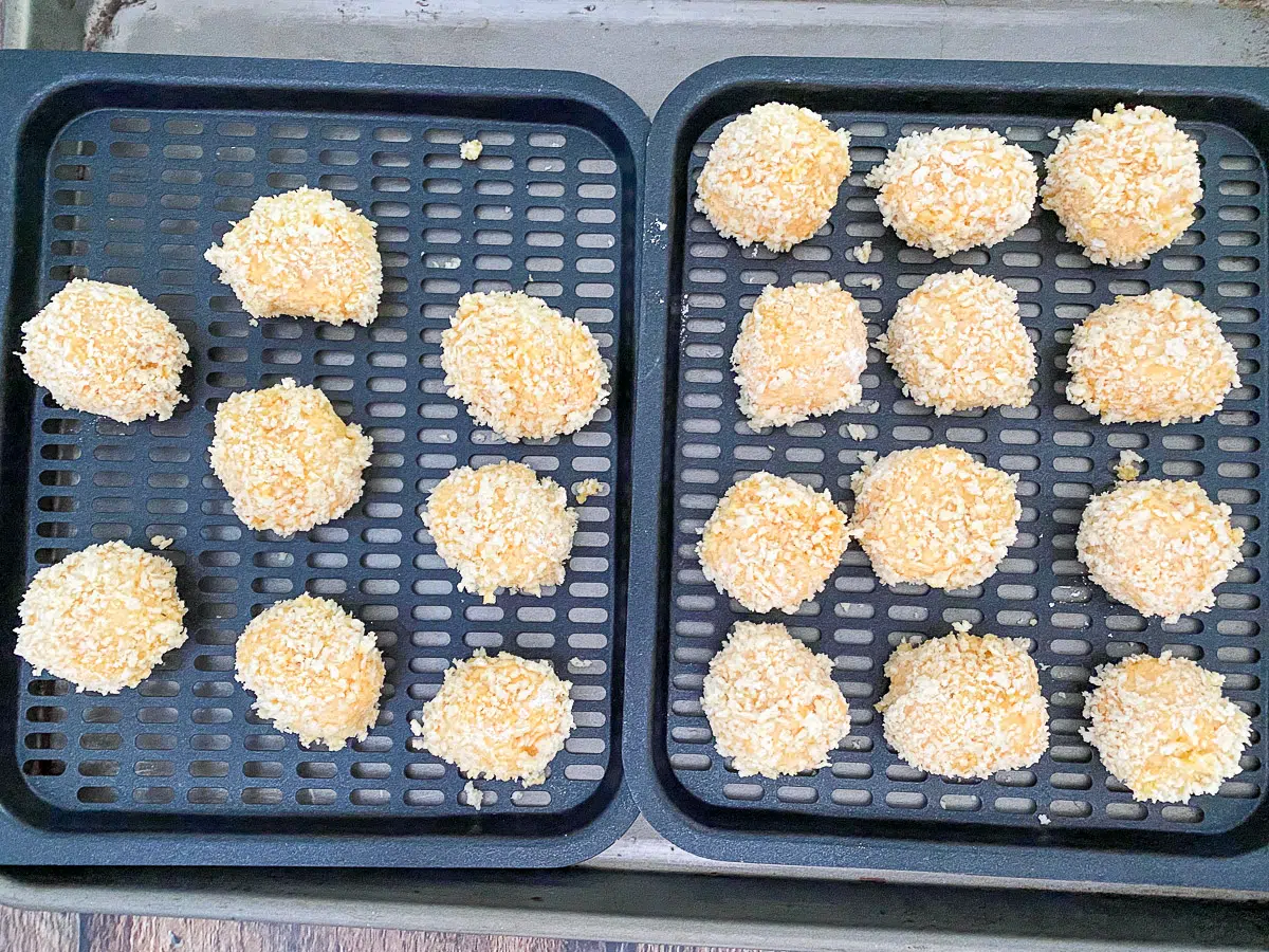 Chicken bites rolled in flour, egg, and panko breadcrumbs on air fryer pans