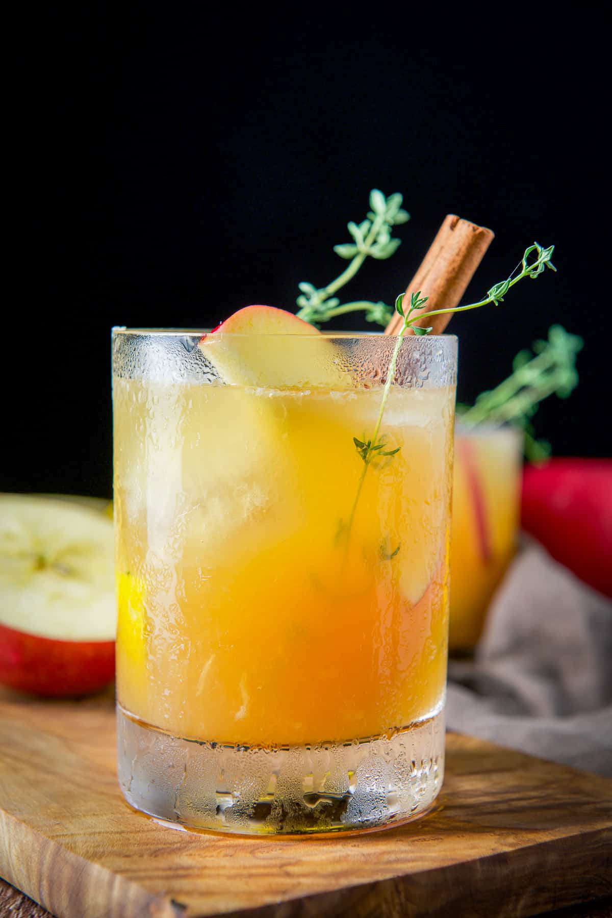 Double old fashioned glass filled with the lemon, apple cider and bourbon, with apple, cinnamon and thyme as garnish