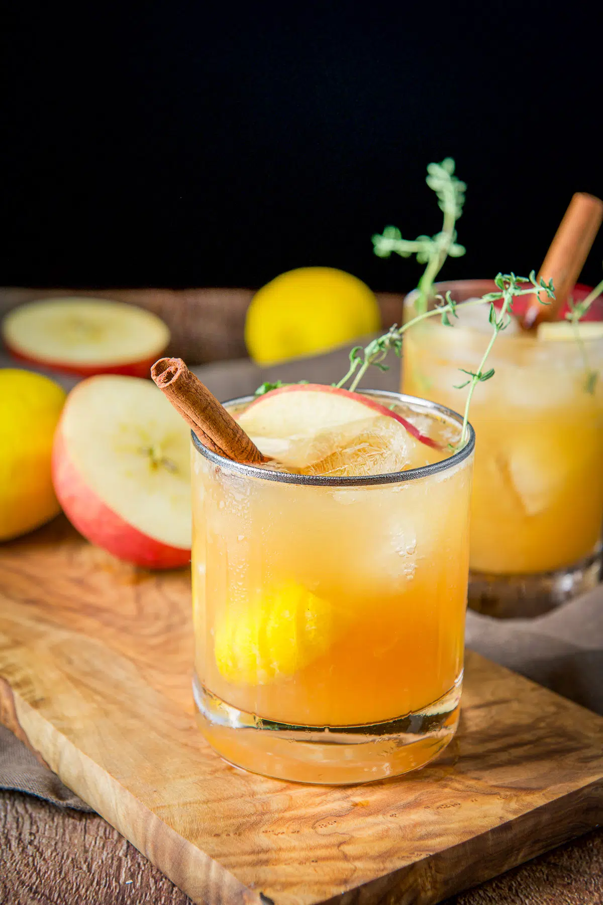 two glasses with the apple cider bourbon smash with apples, lemon and cinnamon sticks in them