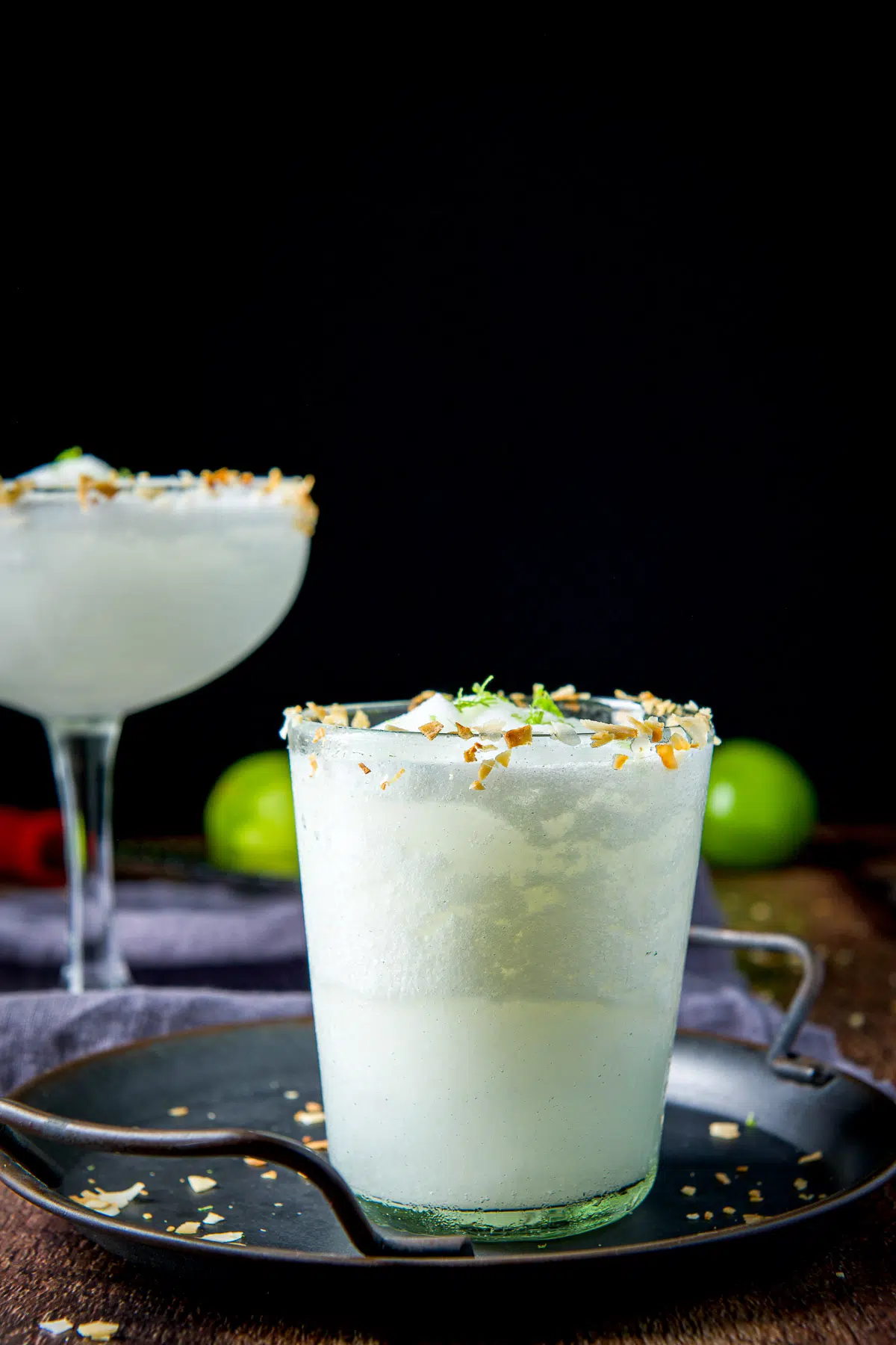Vertical view of the coconut margaritas on a tray with limes in the back