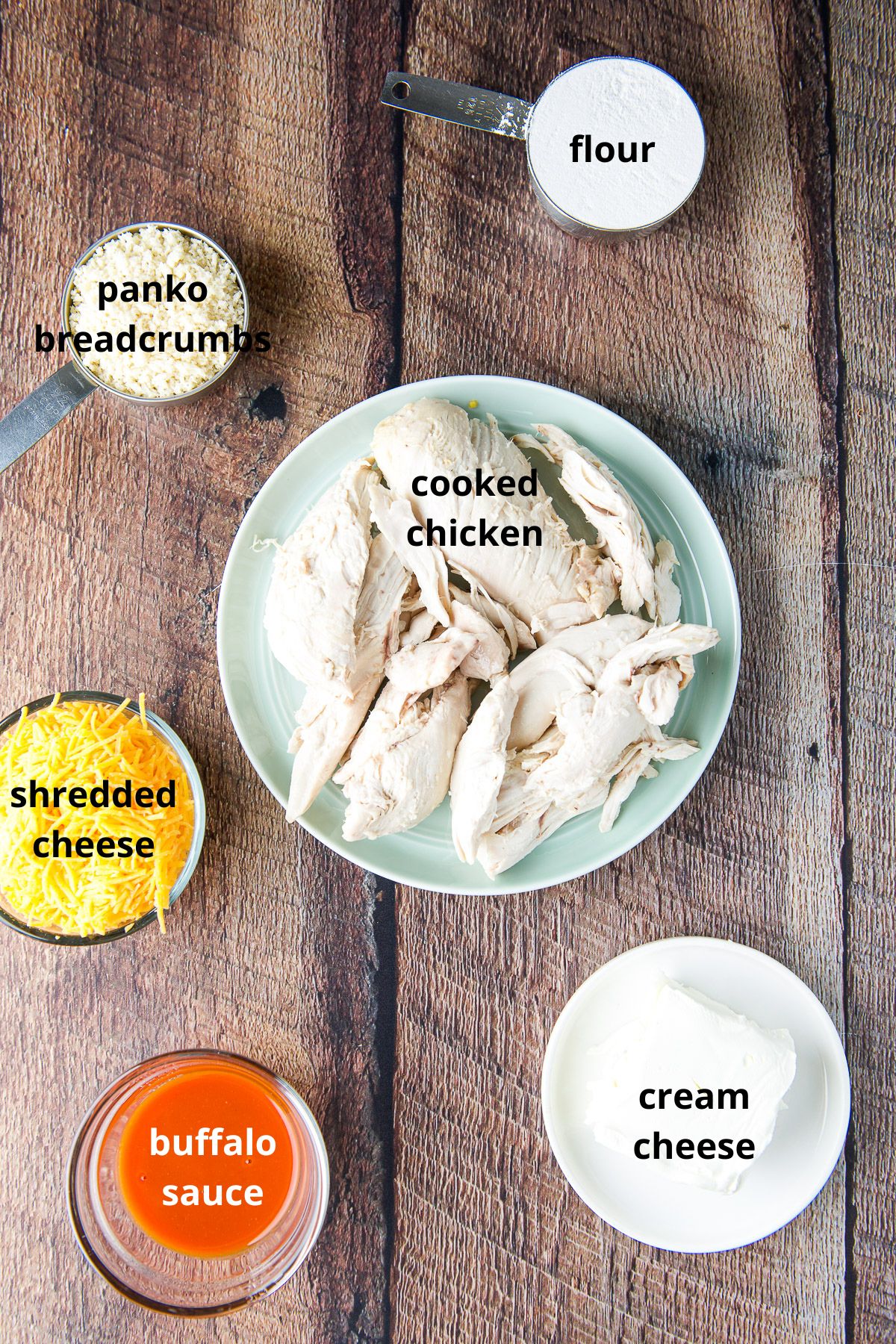 Chicken, breadcrumbs, cheese, buffalo sauce, cream cheese, egg and flour on a table
