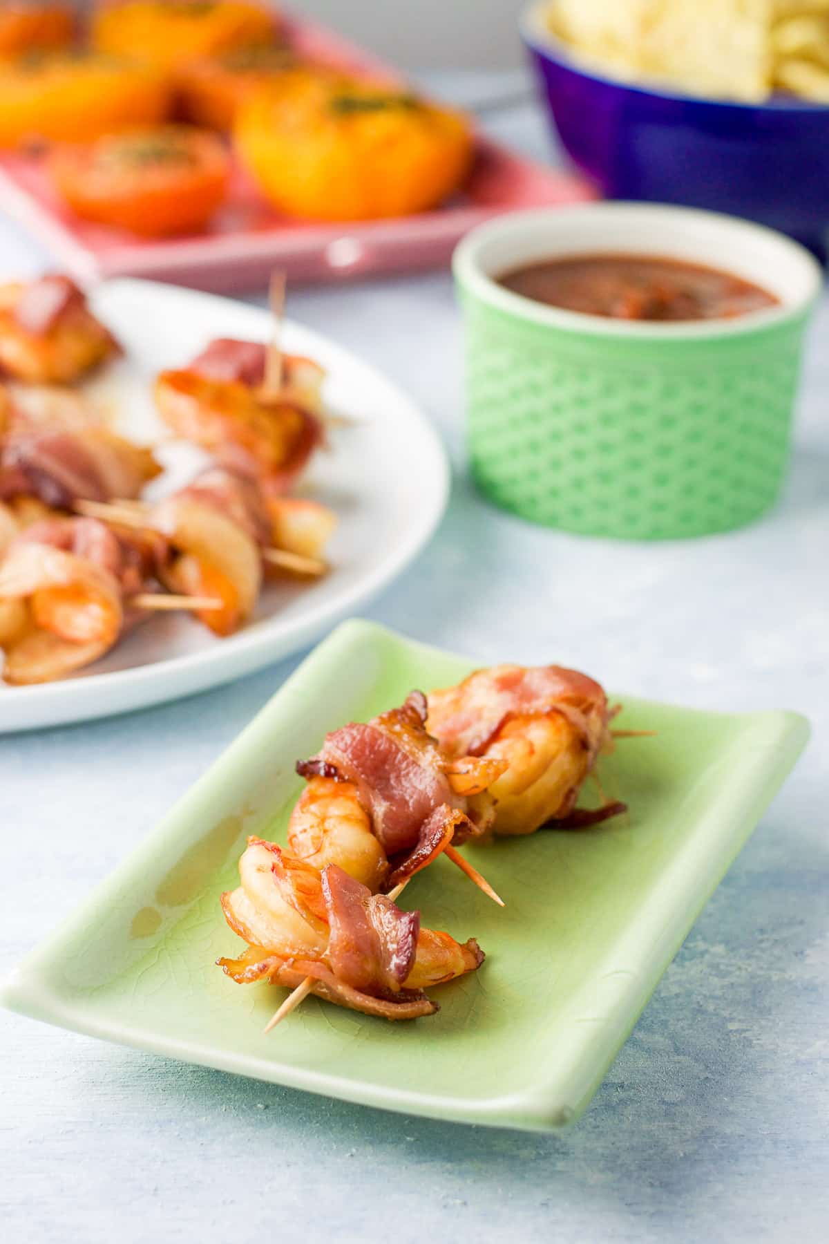 A green plate with three shrimps on it with a plate of them in back