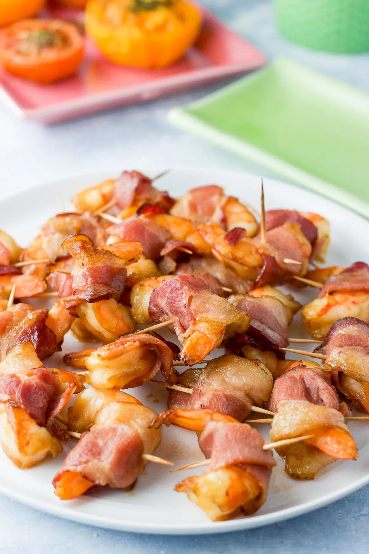 Shrimp wrapped in bacon on a white plate in front of tomatoes
