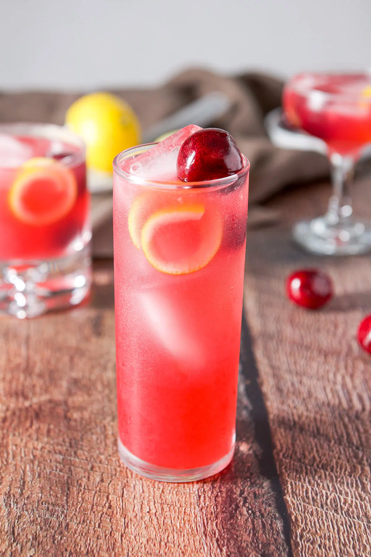Three glasses filled with the cherry sour with cherries and lemon twists in the glasses