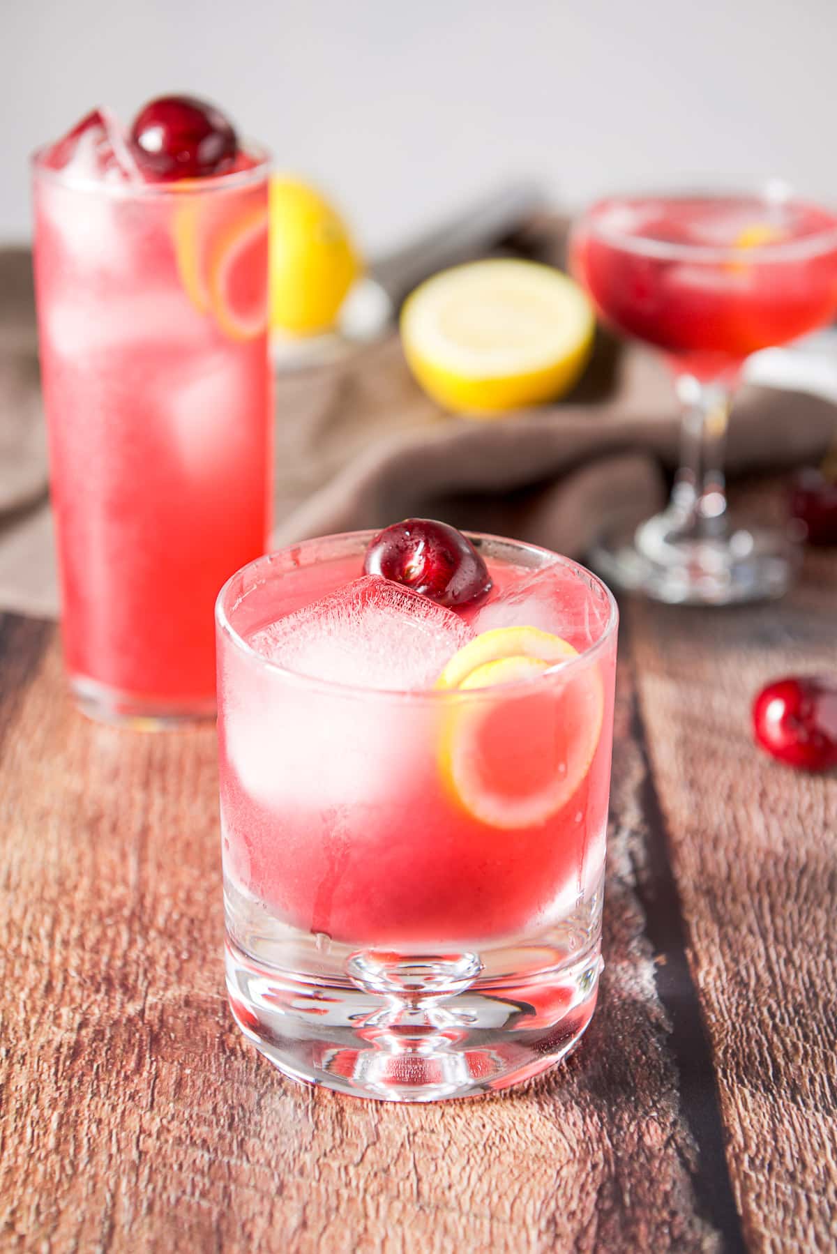 Short glass filled with the pink cocktail with two other glasses behind