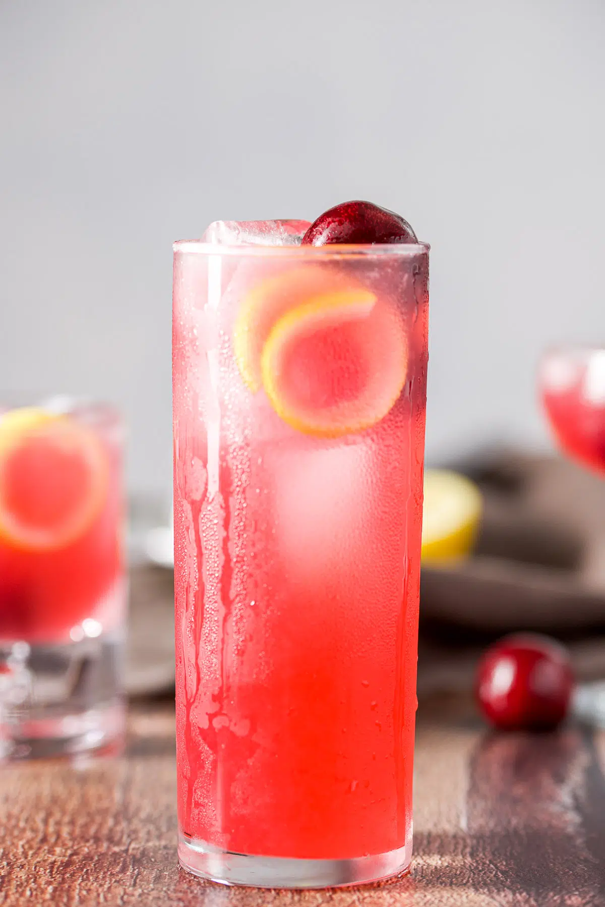 tall thin glass with the vodka sour in it with cherries and lemon twists as garnish