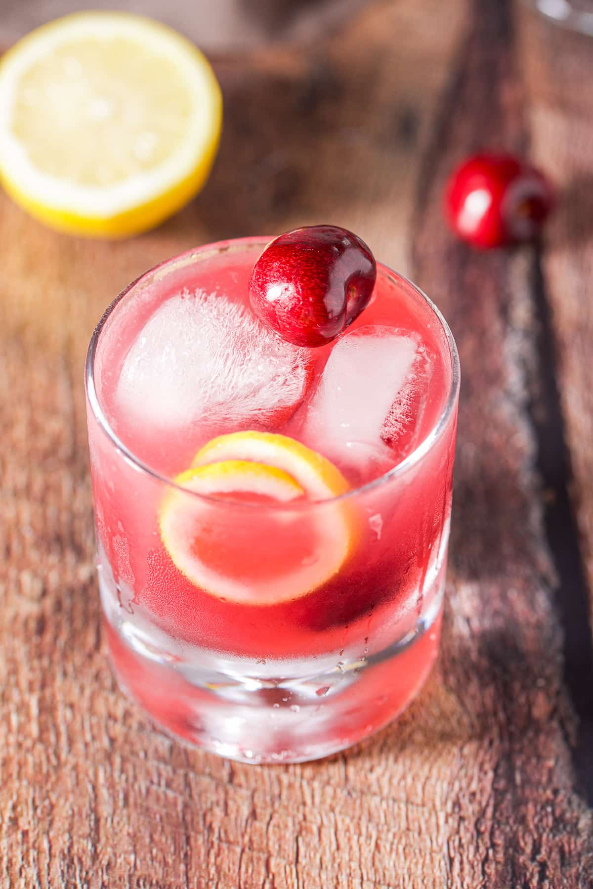 Cherry sitting on some ice in a glass with the pink cocktail