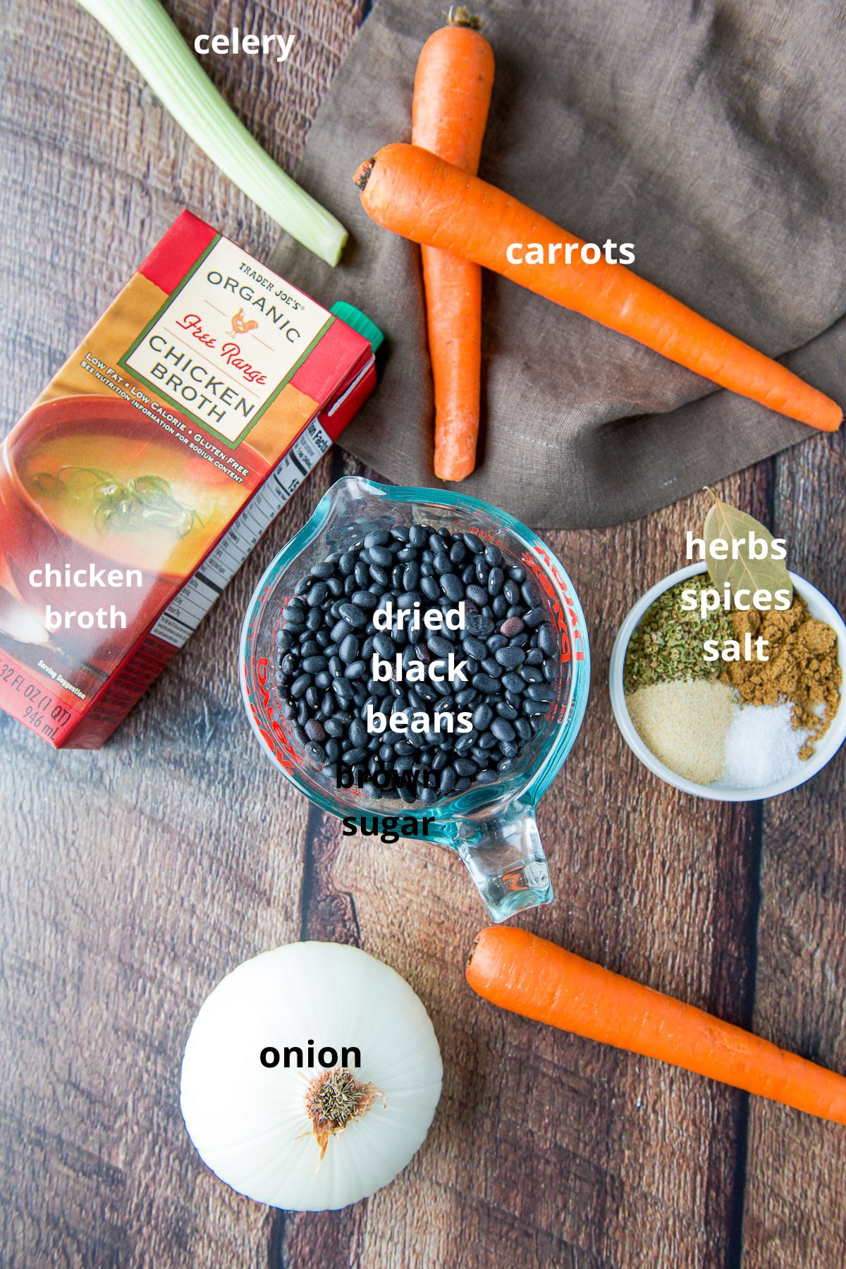 Black beans, onion, herbs and spices, broth, celery, and carrots on a table