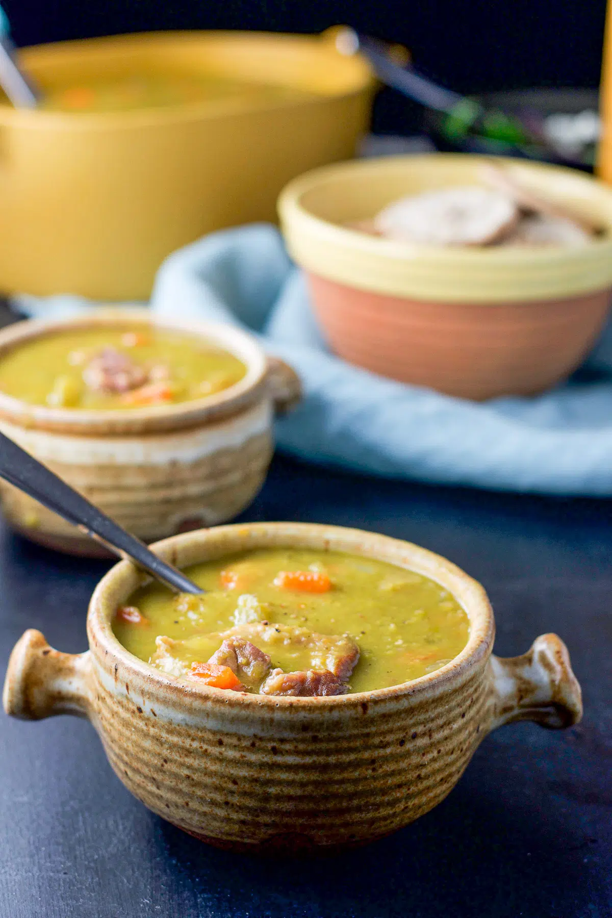 two crocks filled with pea soup with a serving bowl behind it