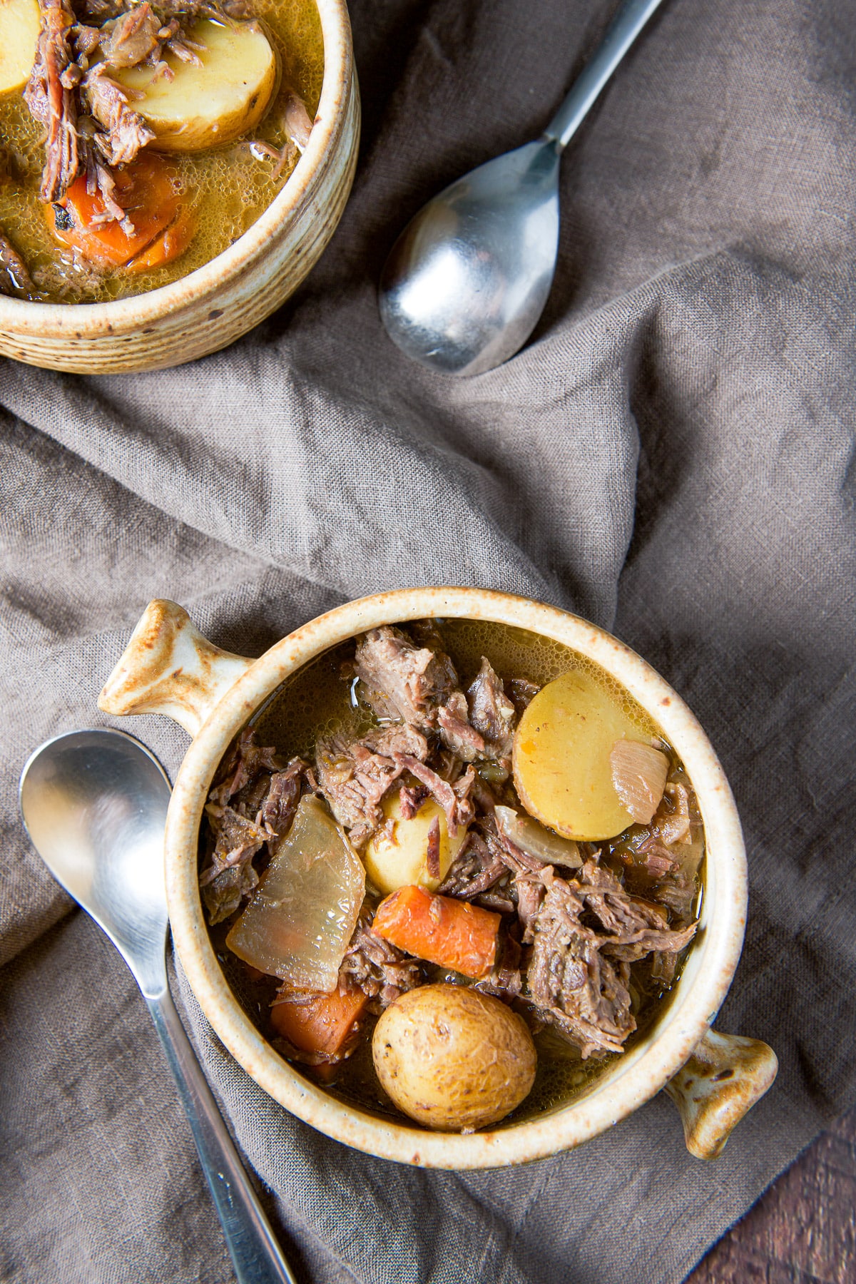 Overhead view of the two crocks filled with the hearty stew with two spoons