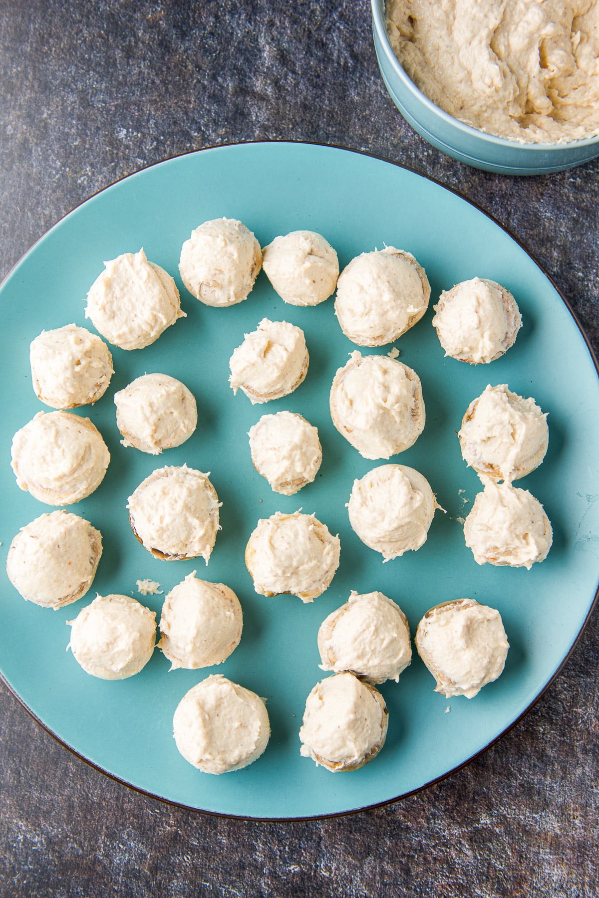 Overhead view of the stuffed mushrooms on a plate with the filling in a bowl