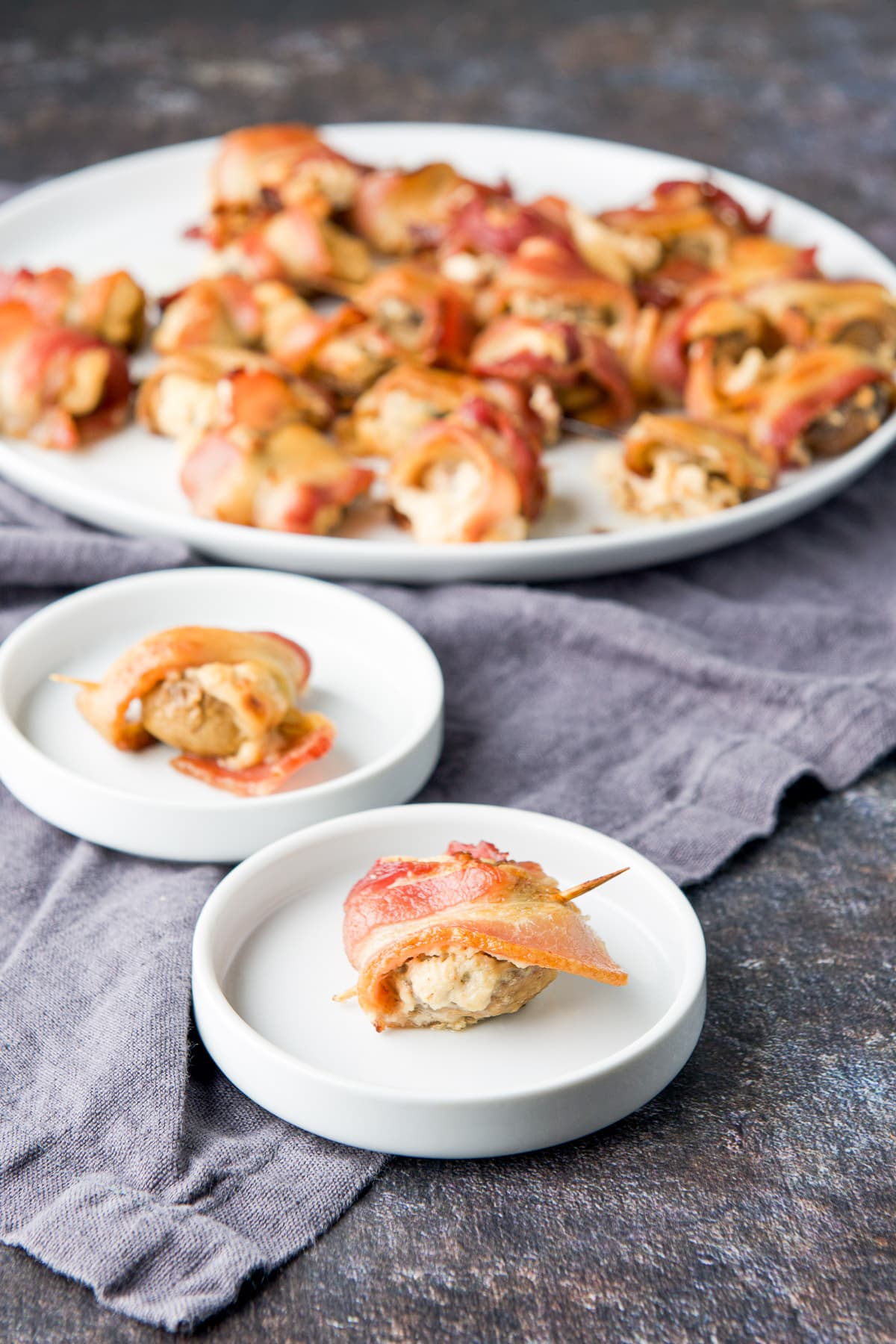 Two small white plates with stuffed mushrooms wrapped in bacon with the big plate in back