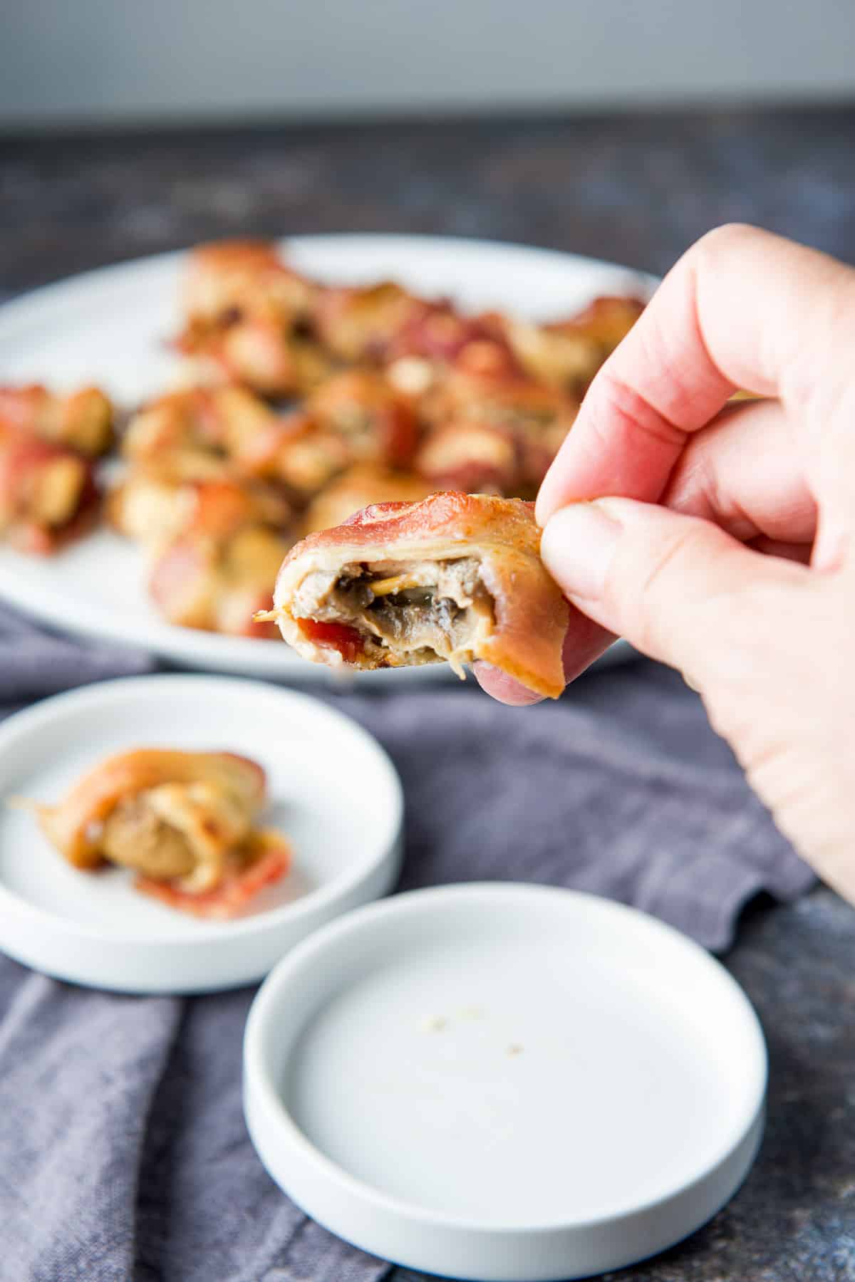 A hand holding a bacon mushroom with a bite taken out of it
