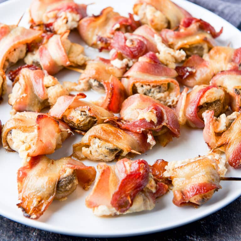 square photo of a plate of stuffed mushrooms in bacon