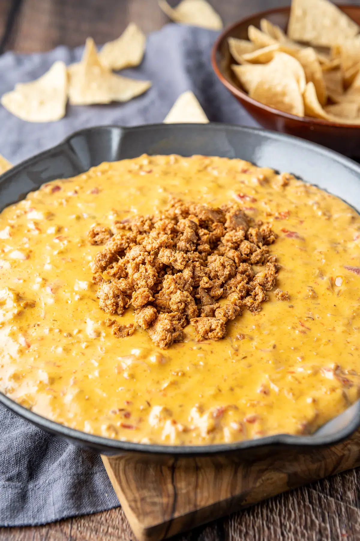 A large skillet with the cheesy dip with meat on top with chips in back