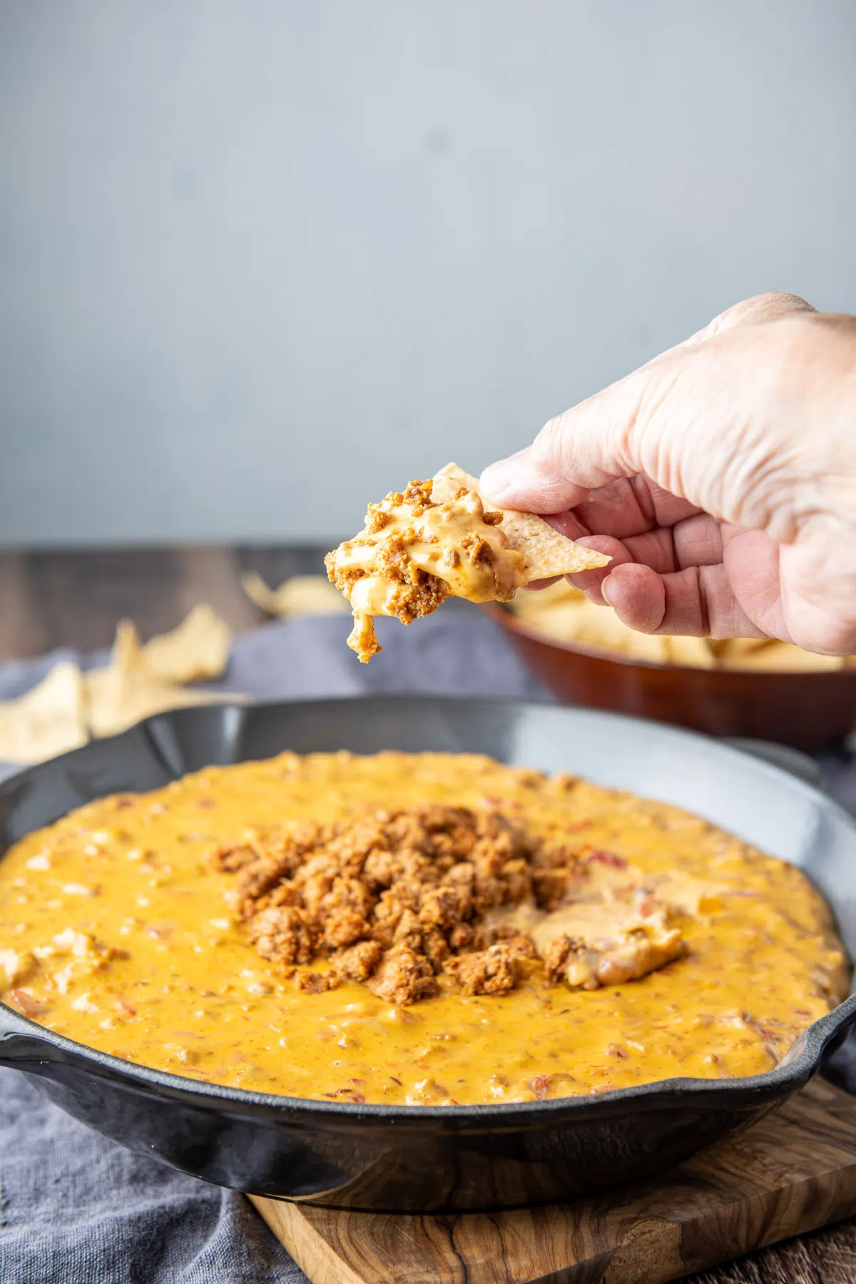 A hand holding a chip with the chorizo dip on it, held over the pan
