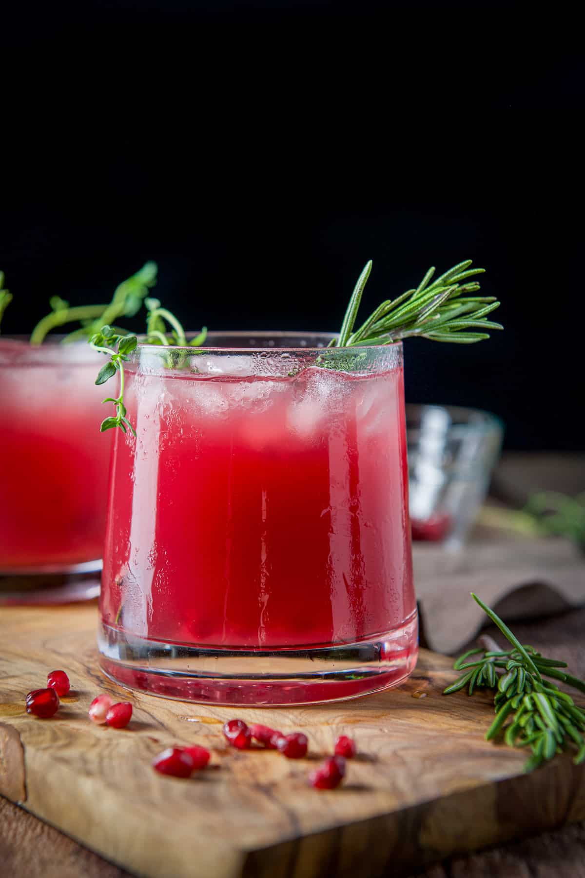 Vertical view of a double old fashioned glass filled with the red drink with thyme and rosemary in it