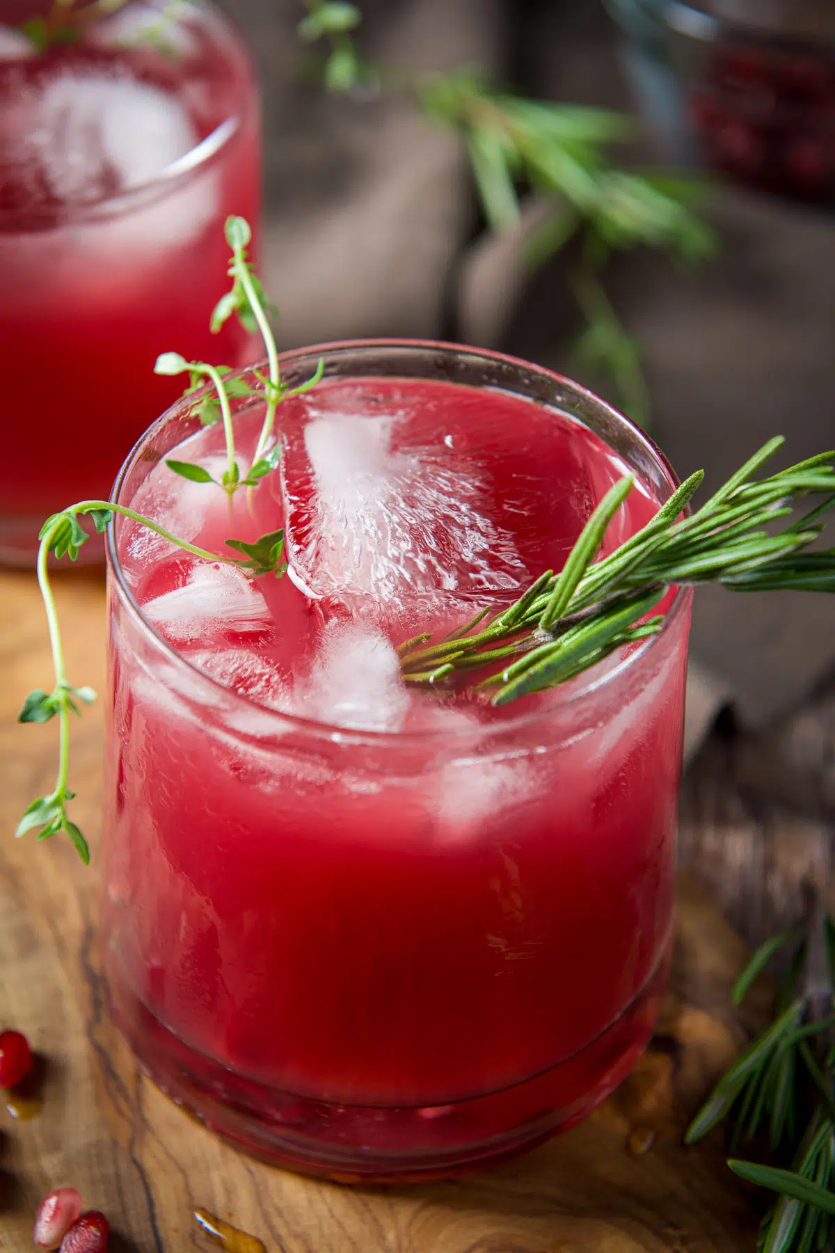 Close up of the red cocktail in a glass with fresh thyme and rosemary