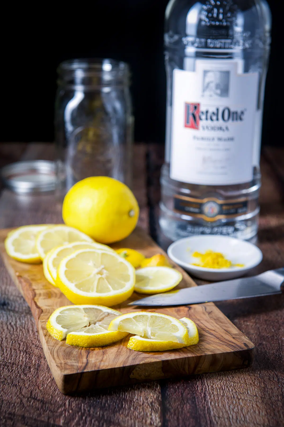 A board with sliced lemon, with zest, and vodka on the table