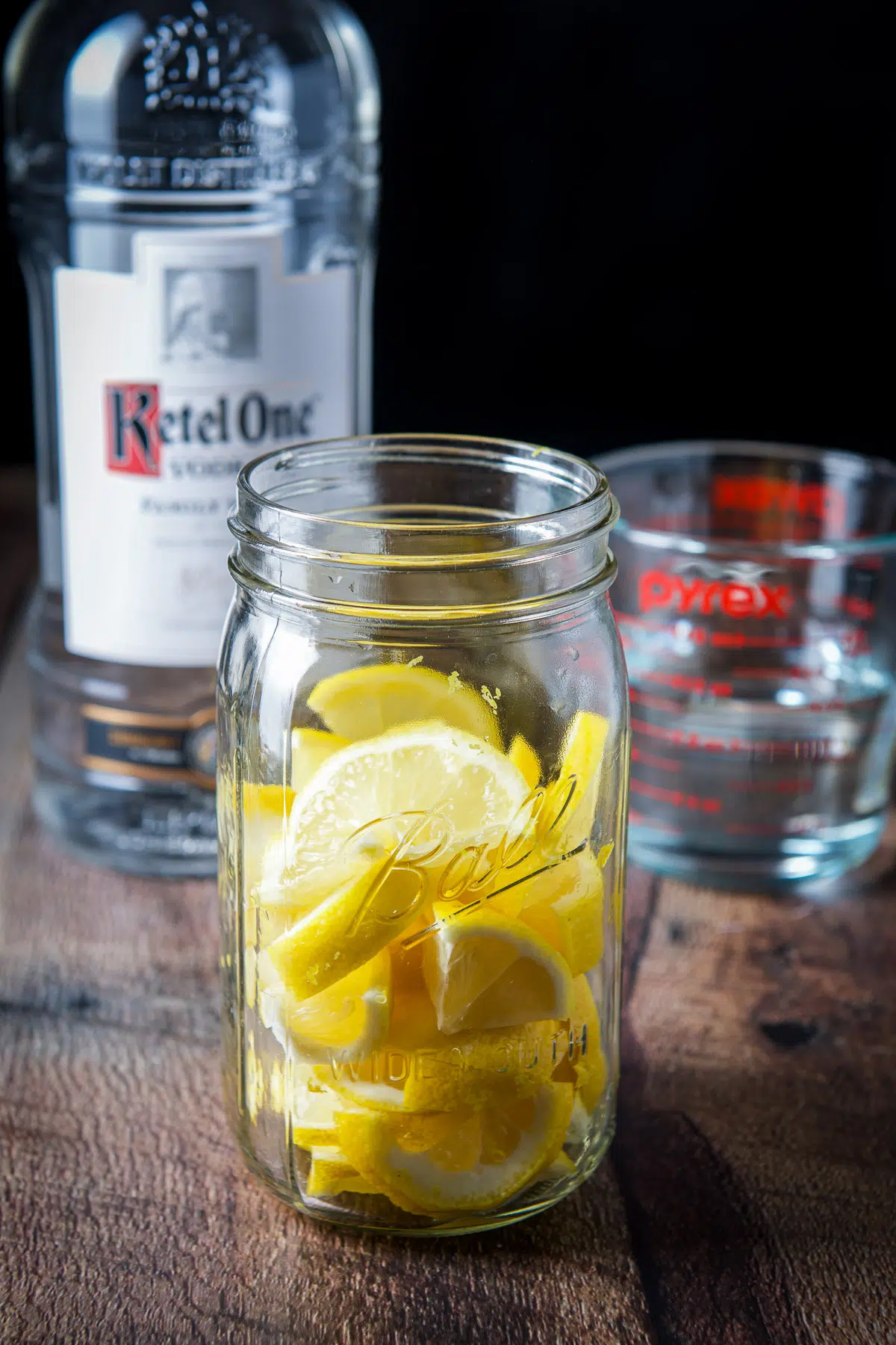 A jar with the sliced and wedges of lemon with vodka in the back