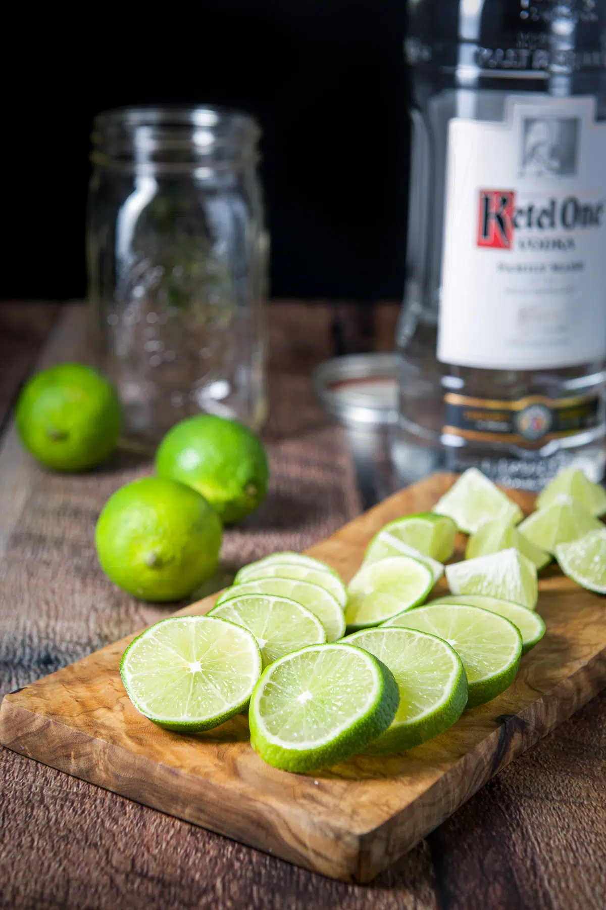 sliced lime and in wedges on a board with more in the back and vodka