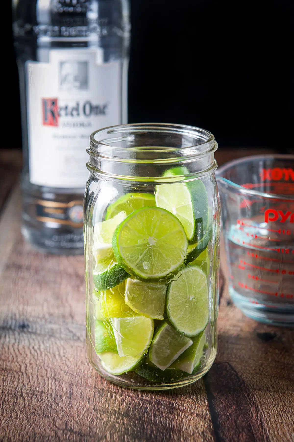 A jar with the sliced lime in it with vodka in back