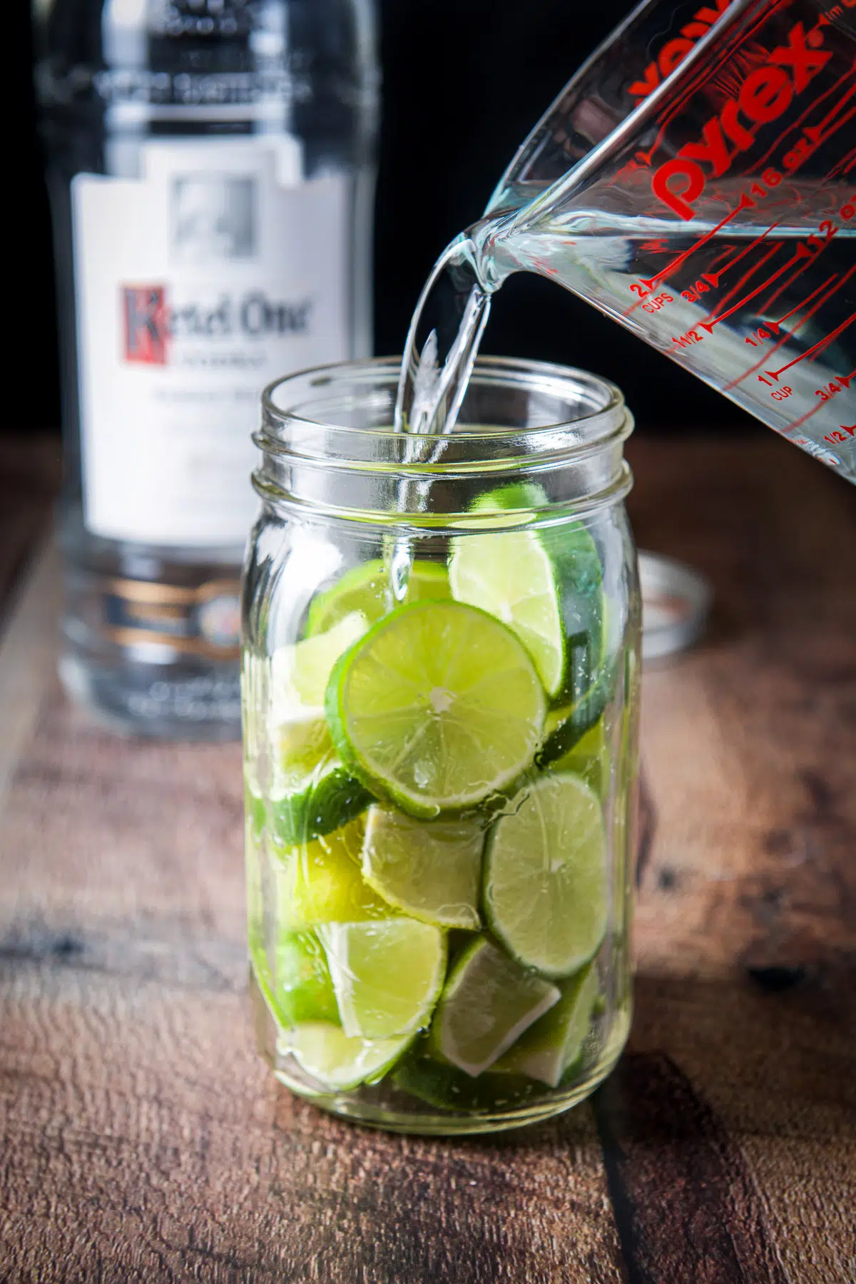 Vodka being poured into a jar of limes