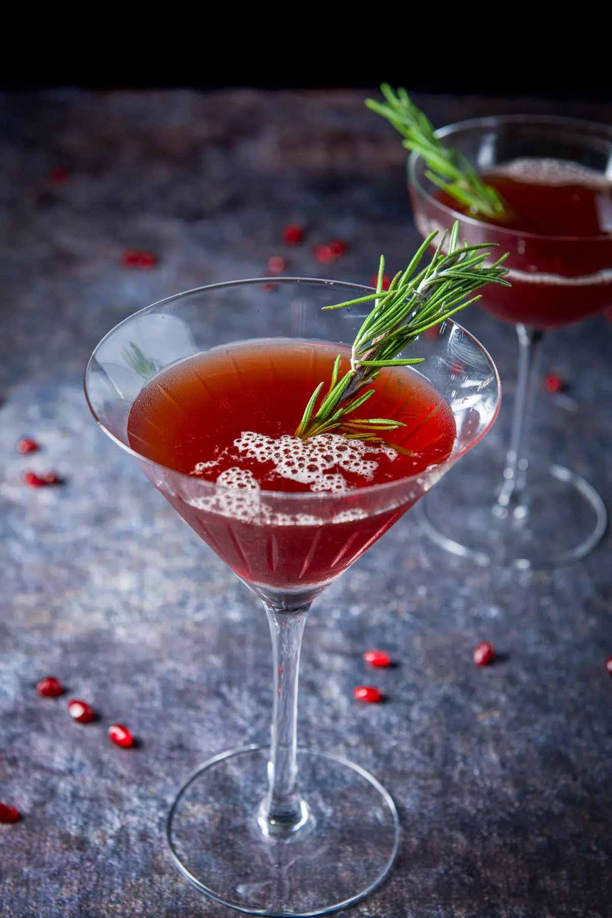 Fluted glass filled with the manhattan with a sprig of rosemary and pomegranate seeds on the table