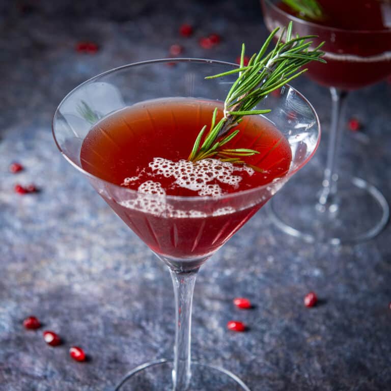 A martini glass with the manhattan in it with pomegranate seeds on the table- square